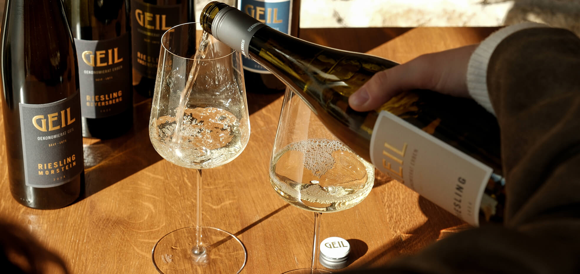 Riesling, der in ein Glas eingeschenkt wird, weitere Rieslingflaschen im Hintergrund
